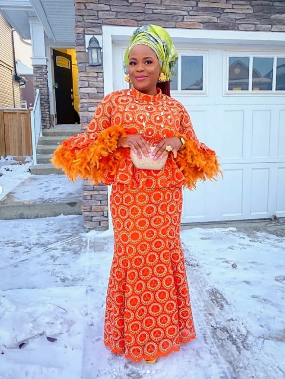 Client wearing an orange lace skirt and blouse with feather sleeves sewn by Jovibest Fashions